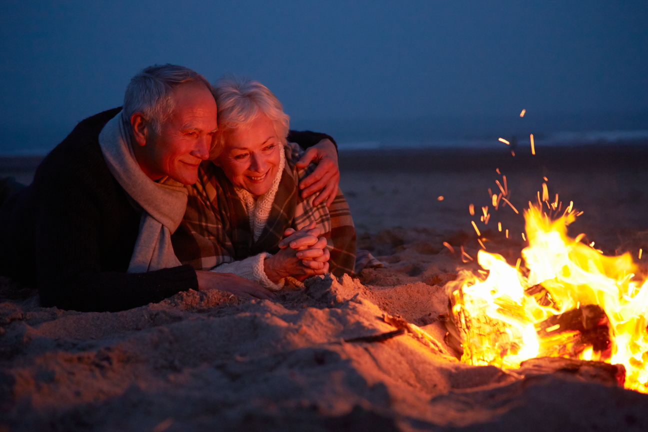 Senior couple sitting by the fire on the beach